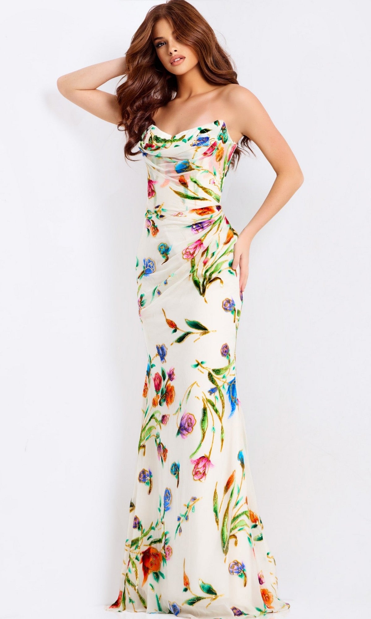A woman poses in the Jovani 47626 Long Prom Dress, which is form-fitting with a colorful floral print, against a plain white background.